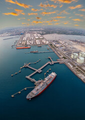 Aerial view of an LNG tanker docked at an offshore terminal with multiple pipelines, storage tanks, and an industrial complex. Captures global energy logistics