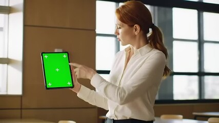 Professional woman presenting a digital tablet with a green screen in a modern office environment - Powered by Adobe
