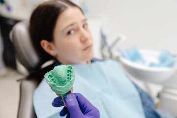 Dentist showing dental mold to young patient in clinic