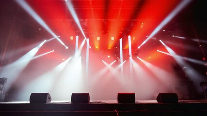 Illuminated stage with red lights and spotlights shining down on a row of speakers below it. Stage lights shine in red. Concert stage with smoke. Lights beam through the mist - Powered by Adobe