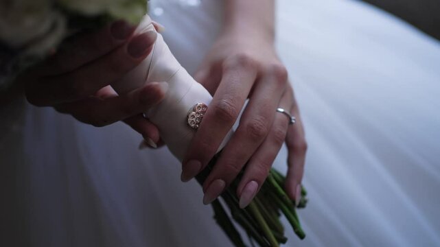 bride&rsquo;s hands holding bouquet wrapped in ribbon with delicate brooch
