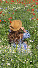 Woman Enjoying a Sunny Day in a Blooming Wildflower Field Wearing a Straw Hat and a Blue Dress With Floral Patterns