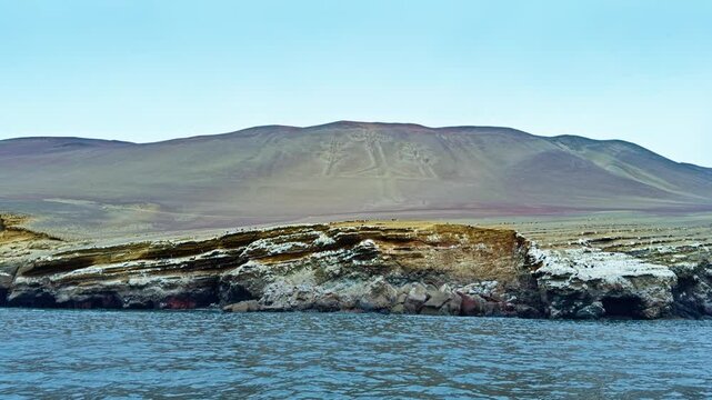 Candelabra geoglyph seen from ocean point with rocky coast in Paracas, Peru, establishing wide overview