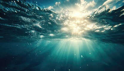 Underwater view of sunbeams piercing through a dark blue ocean surface, creating a dramatic contrast between light and shadow