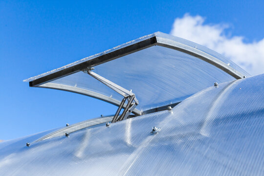 An open automatic ventilation vent on modern greenhouse - Powered by Adobe