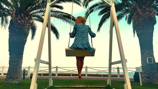 Woman enjoying swing in Tropical beach setting with palm trees