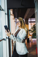 In a modern office, a confident businesswoman skillfully uses her smartphone, showcasing creativity and professionalism, embodying success and determination, and inspiring others around her