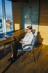 A dedicated professional woman engages in her work remotely from a contemporary office environment, featuring expansive windows that allow plenty of natural light to illuminate the space