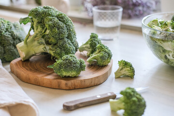 Fresh broccoli florets on a wooden cutting board with a knife ready for cooking highlighting...