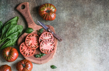 Rustic composition of sliced and whole heirloom tomatoes, fresh spinach, basil, and a knife on...