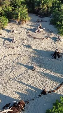Aerial view of beach with concentric circles and teepee structures near lush green vegetation area
