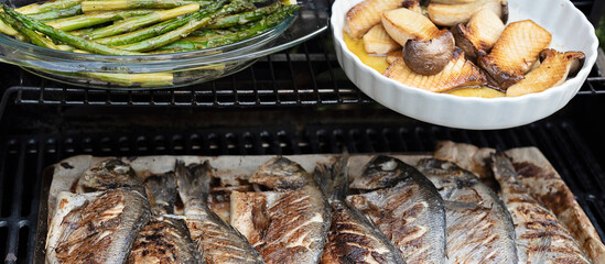 Grilled fish on the grill. Delicious sea bream with asparagus ready to eat for lunch or main dinner. Preparing and grilling during garden party. Cookout. Close up. Panoramic.