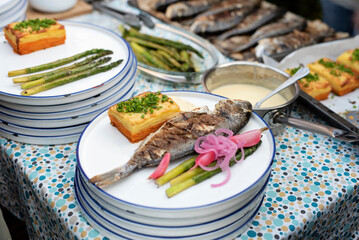 Grilled fish with vegetables and gratin with sauce on plate. Preparation food on a table for lunch on barbeque. Healthy mediterranean meal during garden party or in restaurant. Close up.