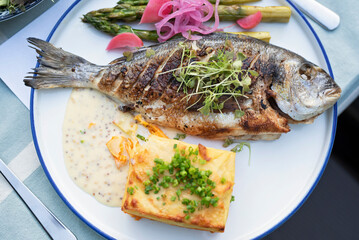 Grilled fish with vegetables and sauce on a plate. Delicious healthy food make on grill as a main dinner ready to eat. Gourmet dorada fish in restaurant or barbecue. Top view.