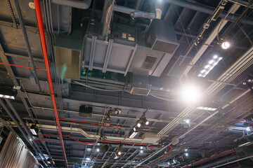 Close-up view of an industrial ceiling with exposed ducts, pipes, and lighting fixtures. The image captures the technical infrastructure inside the Intrepid Museum exhibition space.