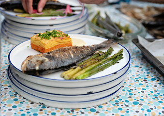 Grilled fish with vegetables and gratin with sauce on plate. Preparation food on a table for lunch on barbeque. Healthy mediterranean meal during garden party or in restaurant. Close up.