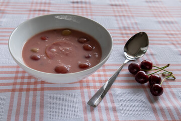 chilled cherry soup with fresh cherries and spoon on checkered tablecloth side view