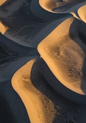 Aerial view of undulating sand dunes creating abstract patterns of light and shadow.