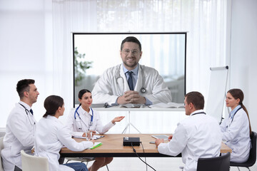 Team of doctors using video projector during conference indoors. Speaker on projection screen