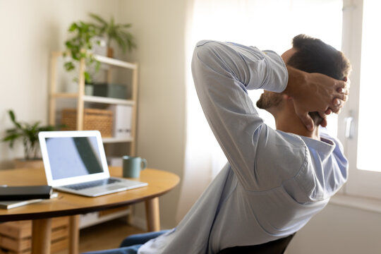 Happy man with hands behind the head relaxing at home office taking a break feeling satisfaction. Copy space.