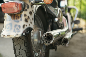 Custom motorcycle rear showcases leopard print fender, chrome dual exhaust mufflers, and rugged...