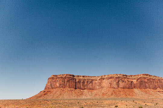 Flat-topped red mesa rises under clear blue sky in Utah desert