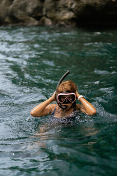 Woman snorkeling in clear tropical ocean water near rocky coastline