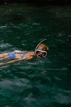 Woman snorkeling in clear tropical ocean water near rocky coastline