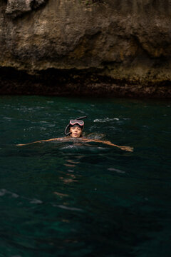 Woman snorkeling in clear tropical ocean water near rocky coastline