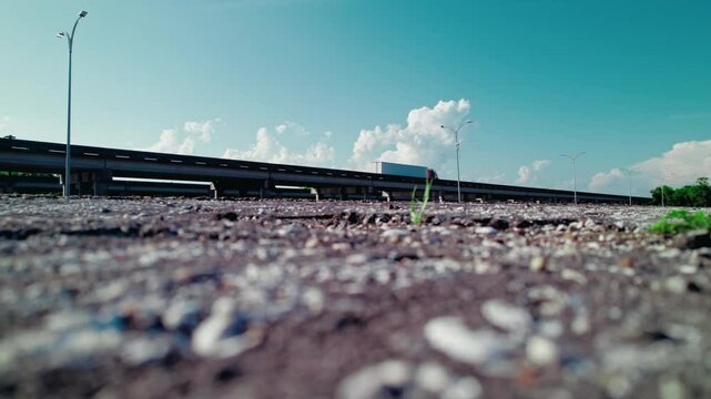 Weed sprouting from a cracked asphalt. Reefer semi-truck cruising over a highway overpass in Laplace, Louisiana, freight logistics.