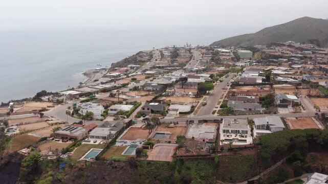 Descending aerial dolly shot of cleared residential lots in the oceanfront Sunset Mesa neighborhood after the Palisades Fire in Malibu, California. 4K