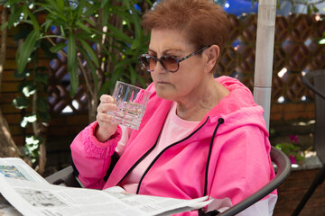 senior woman relaxing on terrace drinking and reading newspaper