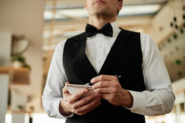 Caucasian young adult man holding notepad and pen standing in restaurant uniform taking order from...