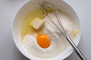 Bowl of flour with a yellow yolk, butter and a metal whisk. Kneading the dough from ingredients for...
