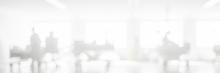 Blurred image of people sitting at desks in a bright office space.