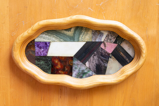 Collection of natural stones such as larimar, hematite, dolomite, skarn, jasper, fluorite and carnelian in polished mosaic in wooden frame as a picture