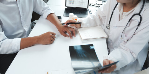 Doctor pointing at patient's wrist injury while examining x ray in medical office