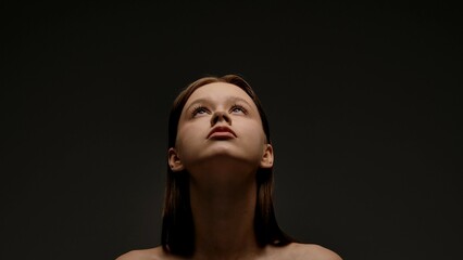 Fototapeta premium Portrait of Woman Looking Up Against Dark Background