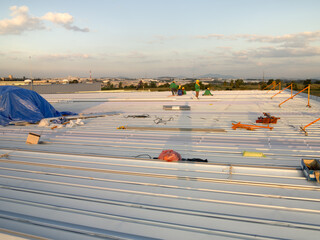 Group of worker to work for metal roof sheet installation in factory warehouse construction site with sky background at evening. Include safety equipment tool i.e. guard rail for prevent high falling.