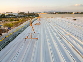 Metal roof sheet installation work for factory warehouse construction project site with sky background at evening. Include safety equipment tool or guard rail and rope for prevent worker falling from