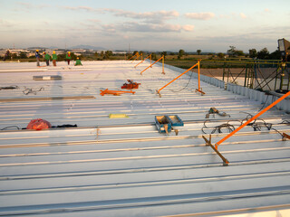 Group of worker to work for metal roof sheet installation in factory warehouse construction site with sky background at evening. Include safety equipment tool i.e. guard rail for prevent high falling.