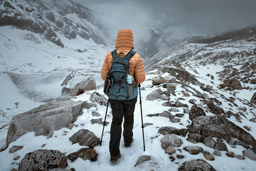Hiker walks along snowy trail through mountain pass against backdrop of an approaching snow storm in Himalayas.