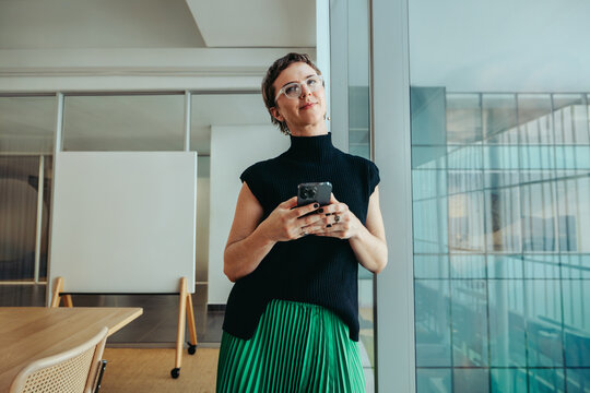 Confident female executive standing in modern office using a smartphone