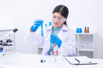 Young girl in goggles analyzing blue liquid sample in test tube during science experiment. Science,...