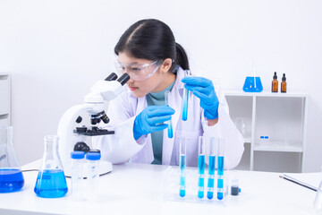 A young Asian female scientist wearing a lab coat and gloves examines samples using a microscope in...