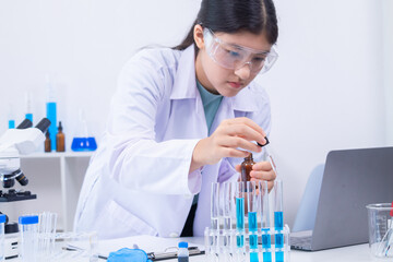 Teen scientist girl conducting science test by carefully evaluating blue solution in laboratory....