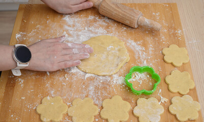 A cook cuts out shortbread cookies from raw dough using a plastic cutter.