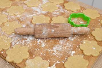 There is a wooden rolling pin on the pastry board, and next to it there are shortbread cookies cut...