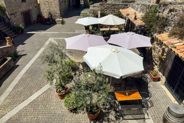top view of charming outdoor cafe with white umbrellas and potted olive trees on a cobblestone...