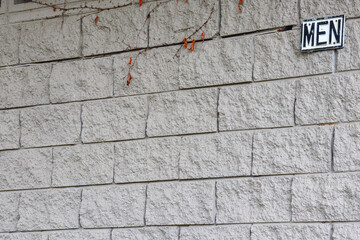 old grey brick wall of public bathroom with men sign
